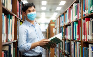asian male student with mask on in library