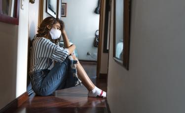 concerned woman sitting at home wearing a mask